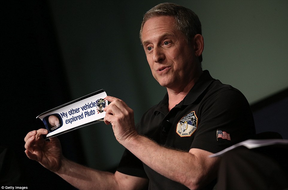 Alan Stern holding a bumper sticker which reads "My other vehicle explored Pluto".